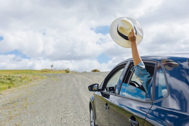 Car driving down a road while a passenger holds a hat out the window