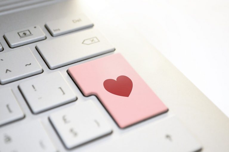 Laptop keyboard with a pink button and a red heart.