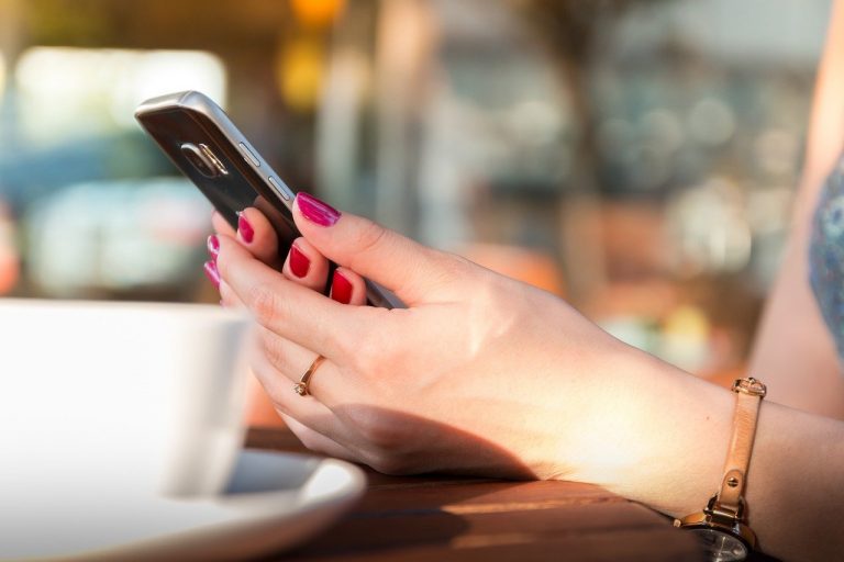 Female holding a cellphone with both hands in a coffee shop